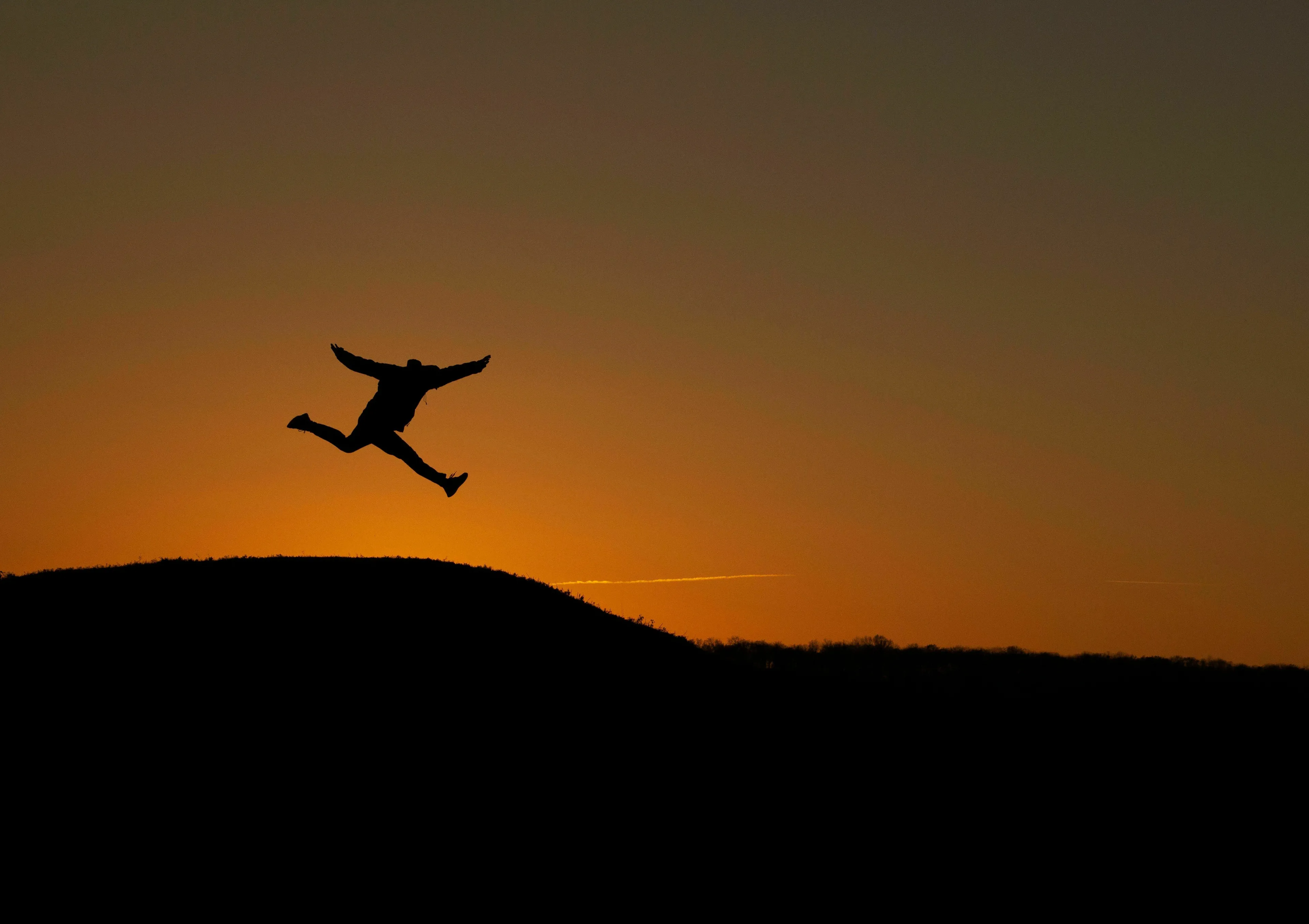 Silhouette of a person mid-air, leaping against an orange sunset, spending their energy, considering extinct species.