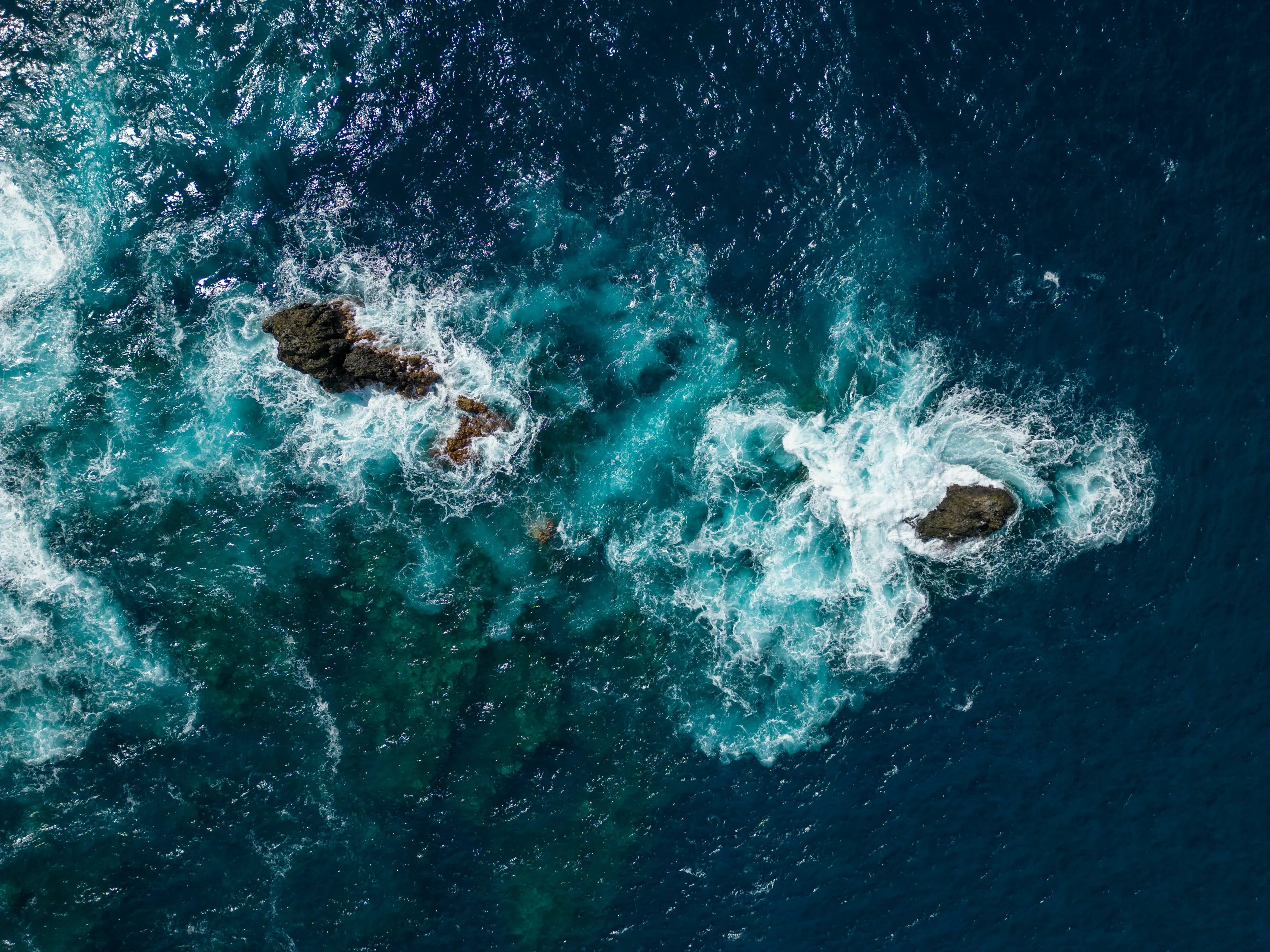 An aerial view of the ocean with waves crashing on rocks, signifying the largest ocean on Earth for a $300 question.