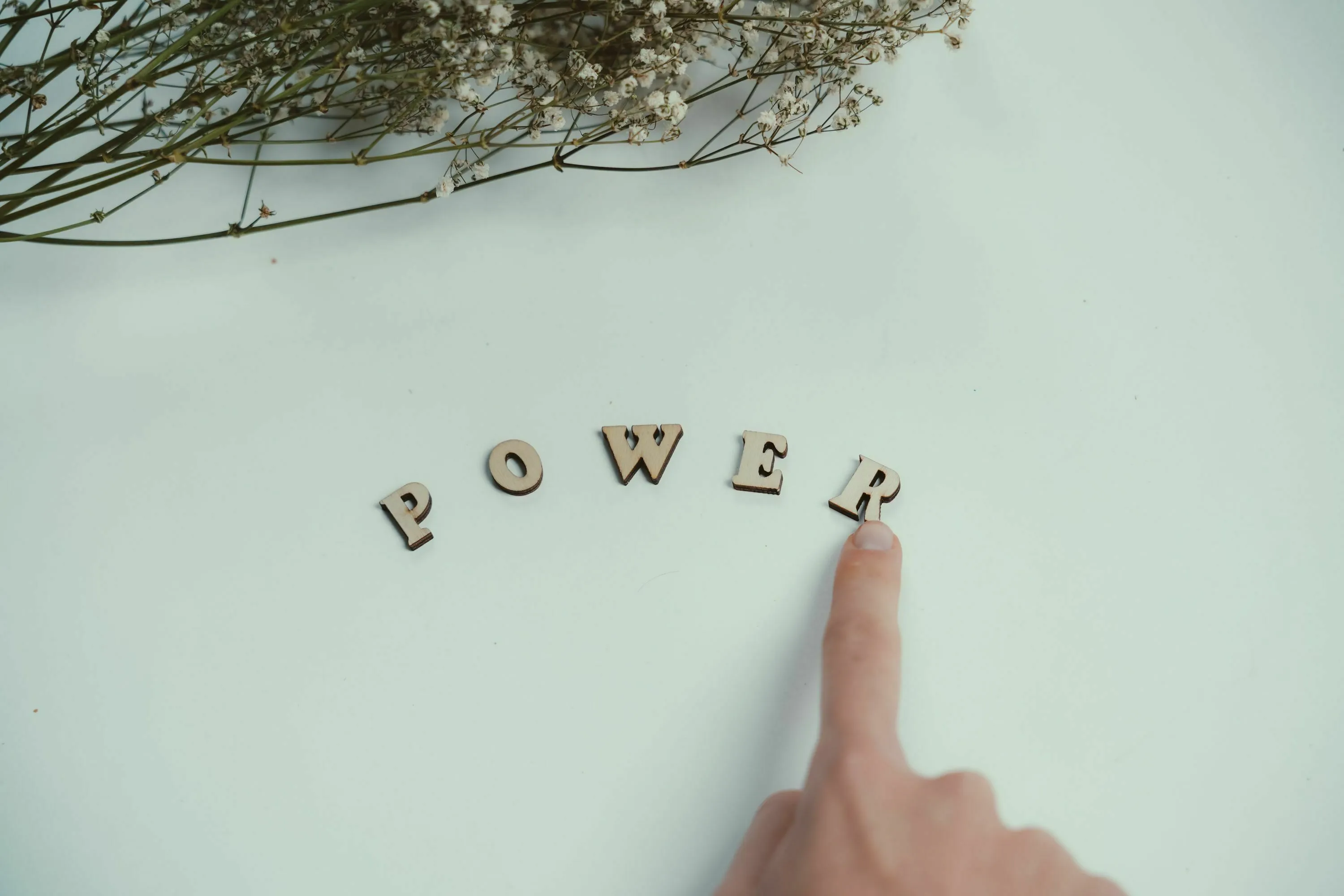 A finger points to wooden letters spelling out POWER on a white surface, representing choosing a superpower.