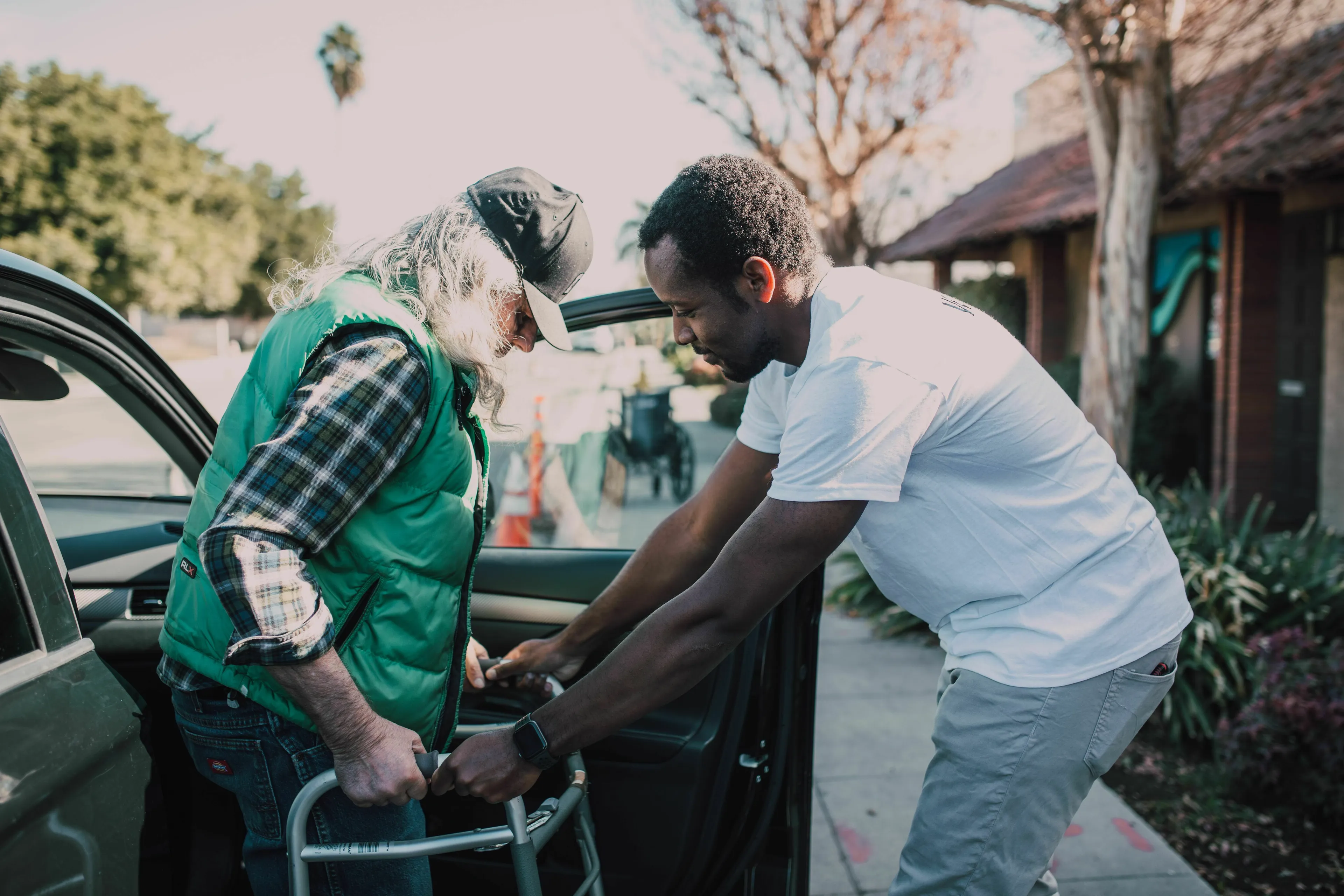 A man helps an elderly person with a walker get out of a car, highlighting the act of seeking validation.