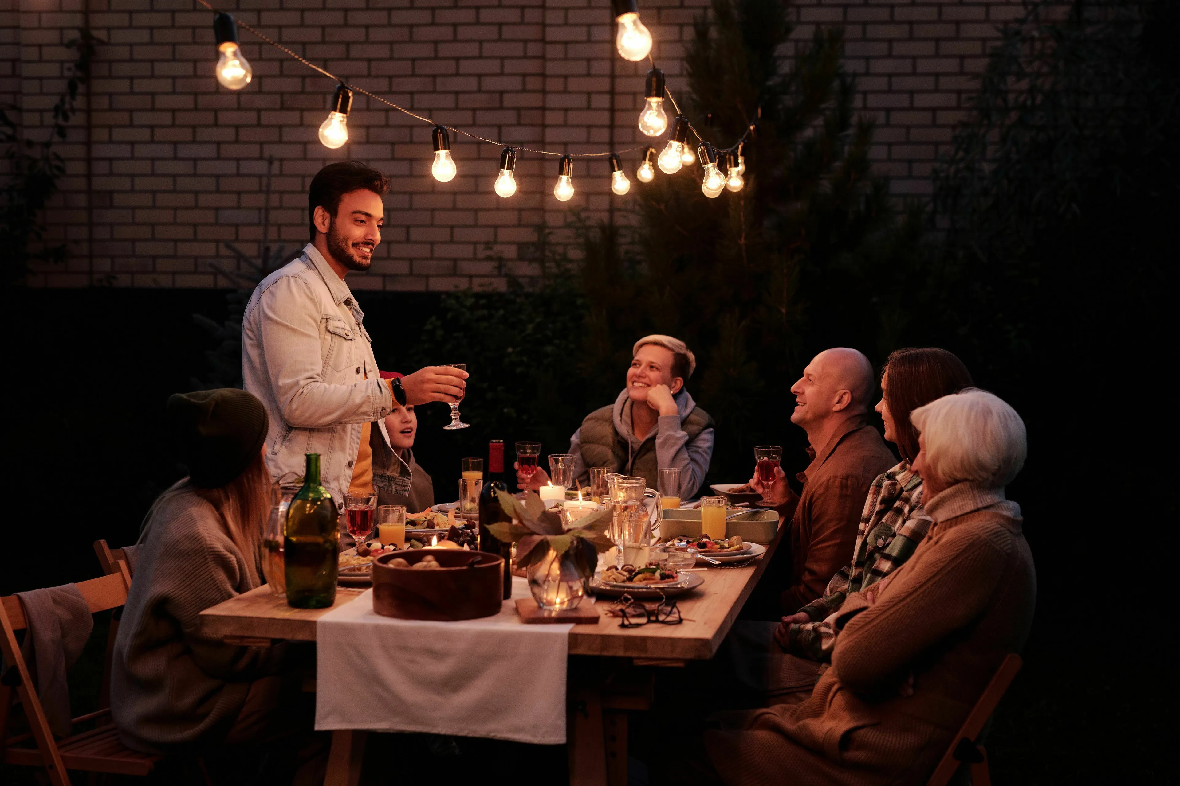 A man stands at a family dinner, talking to smiling family members, illustrating a role in seeking validation.