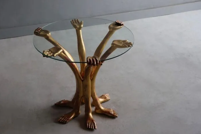 A gold, multi-limbed, bizarre furniture designer glass table on a grey floor.