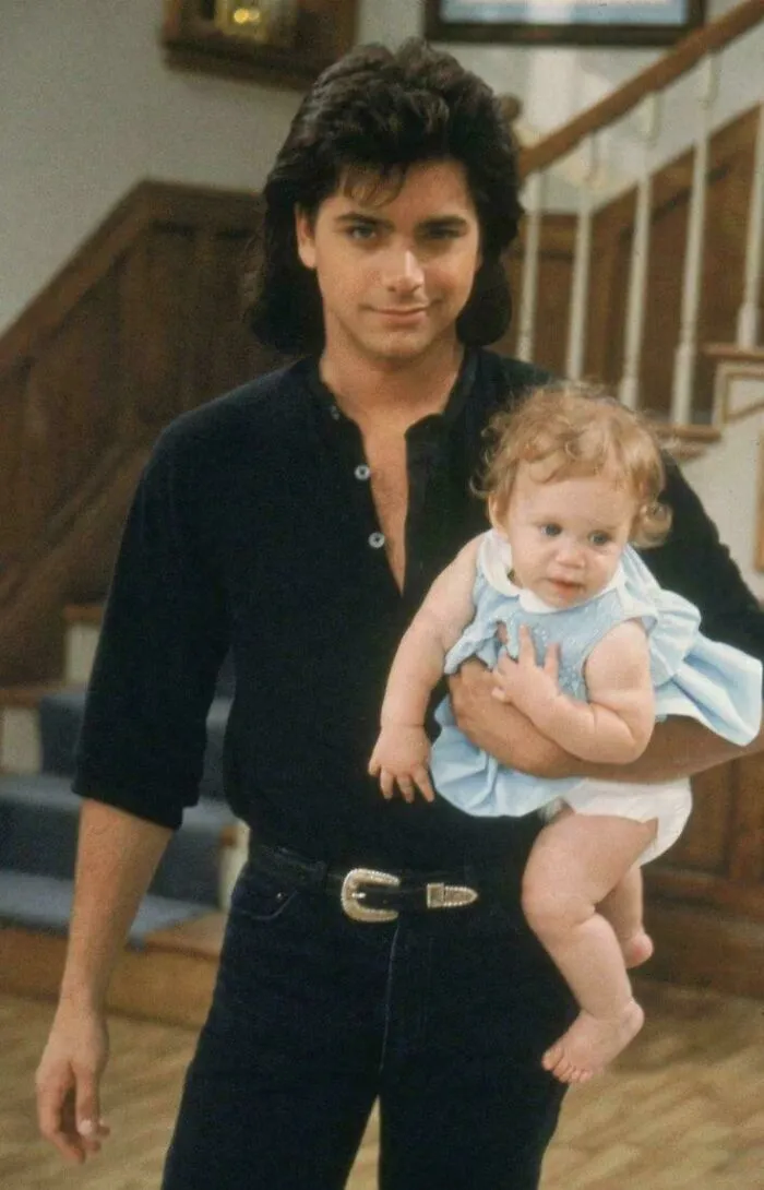 John Stamos holding a baby, a memorable moment that illustrates changing timeline facts.