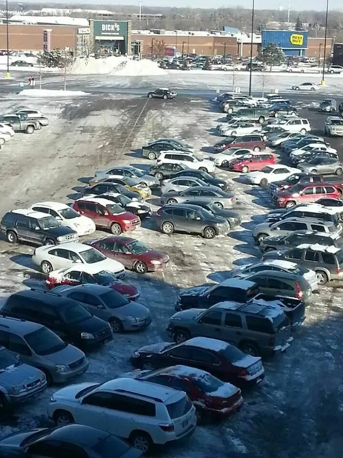 An aerial view of a snow-covered parking lot with cars parked haphazardly, highlighting outrageous parking arrangements.