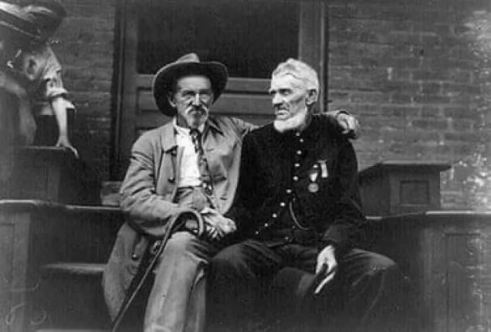Two elderly men, one in a hat and another in a uniform, sitting together on steps, reflecting historical facts.