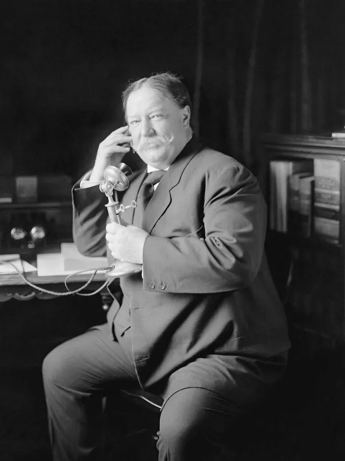 A timeline fact photo of William Howard Taft talking on a candlestick telephone.