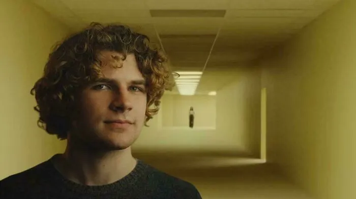 A man with curly hair in a hallway, with a mysterious figure in the distance, representing historical timeline facts.