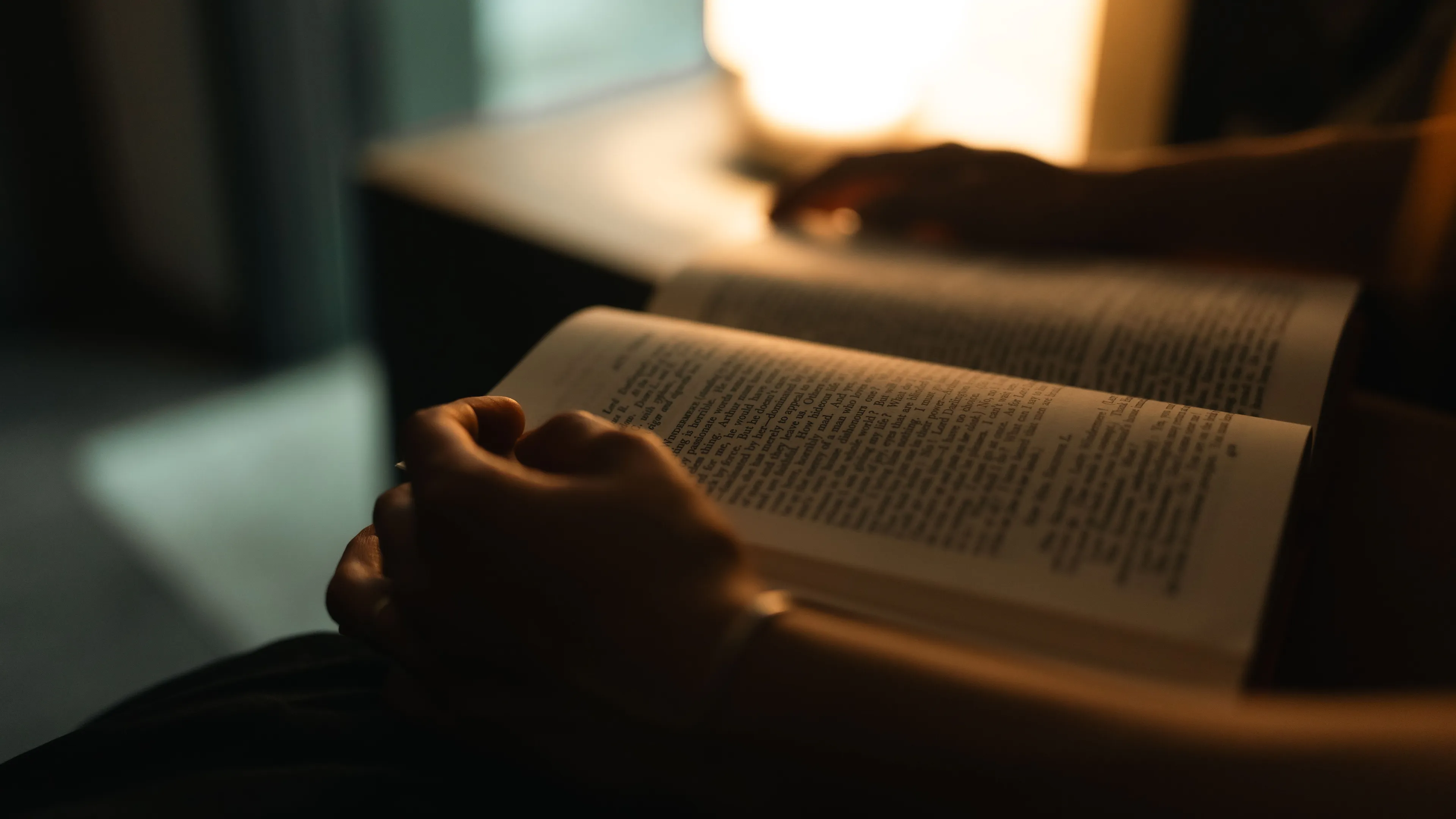 Reading a book during a rainy afternoon, hands holding an open book in a dimly lit room.