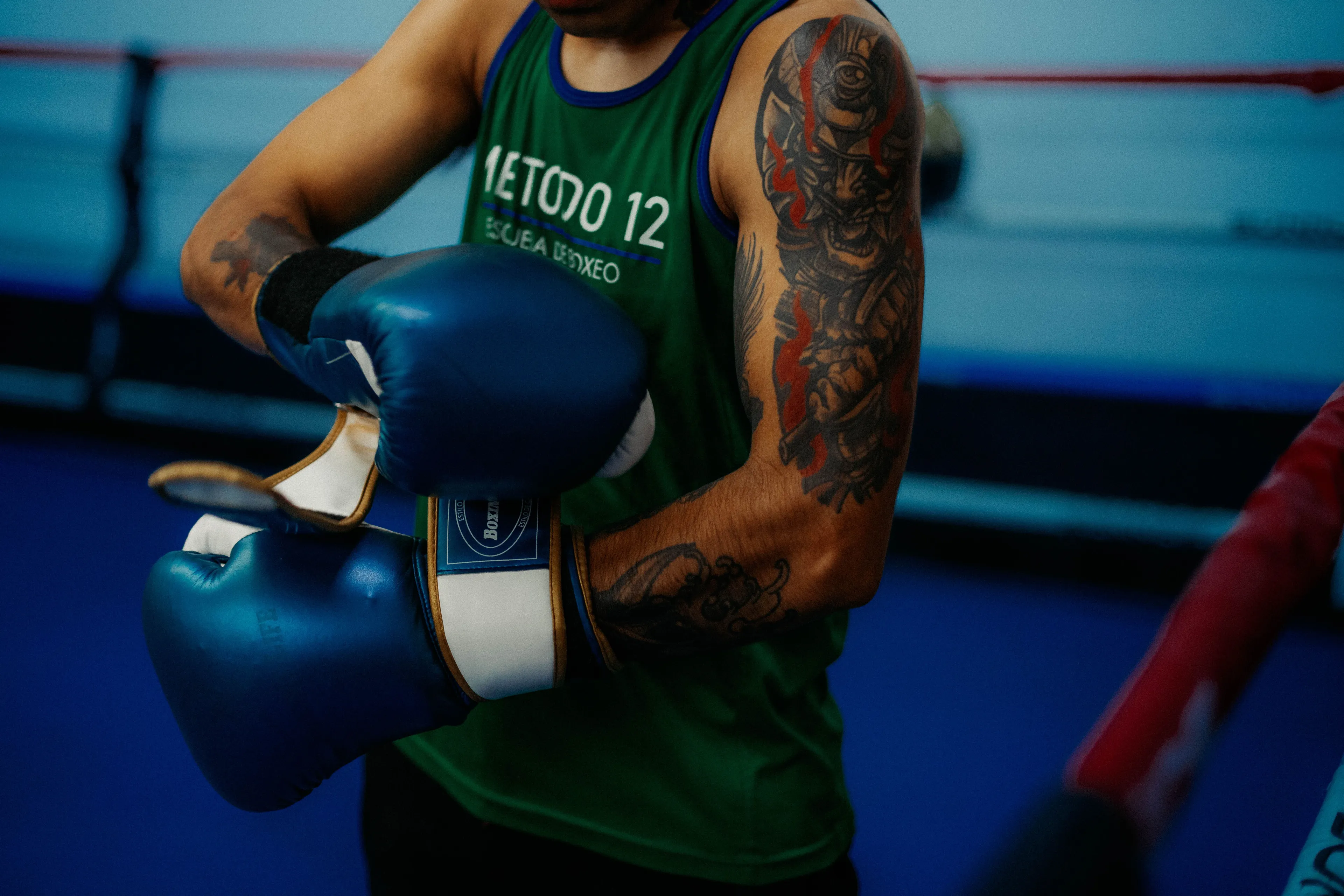 A person with a tattooed arm putting on blue boxing gloves, demonstrating their boxing hobby.