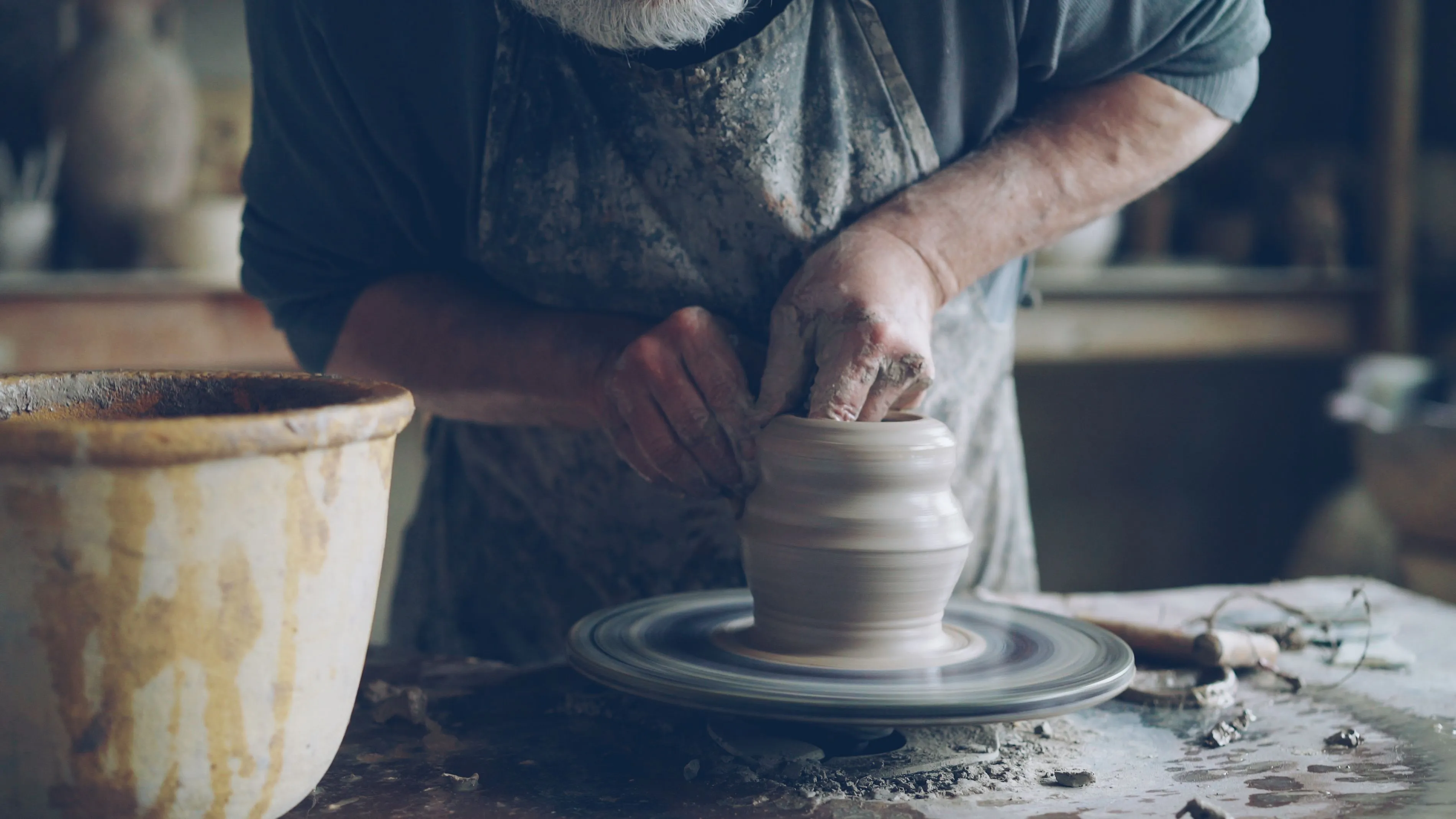 A person's hands are shaping clay on a pottery wheel. Pottery is a creative hobby to master.