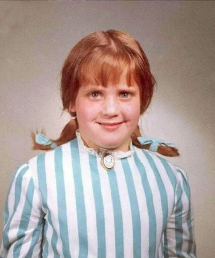A young girl with red hair in pigtails, wearing a blue and white striped dress, smiling. A timeline fact about sense of history.