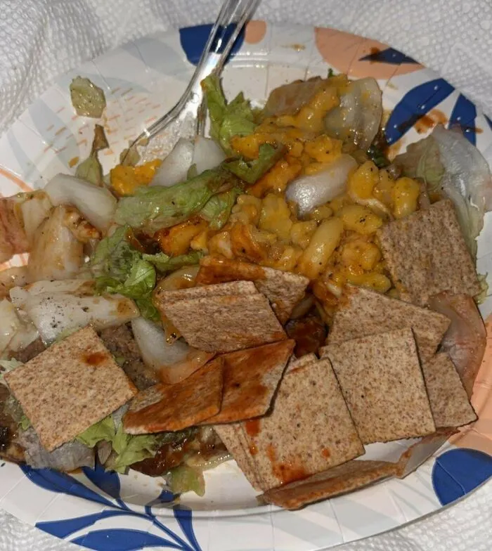 A paper plate with a messy mix of disgusting food, including lettuce, onions, and crackers.