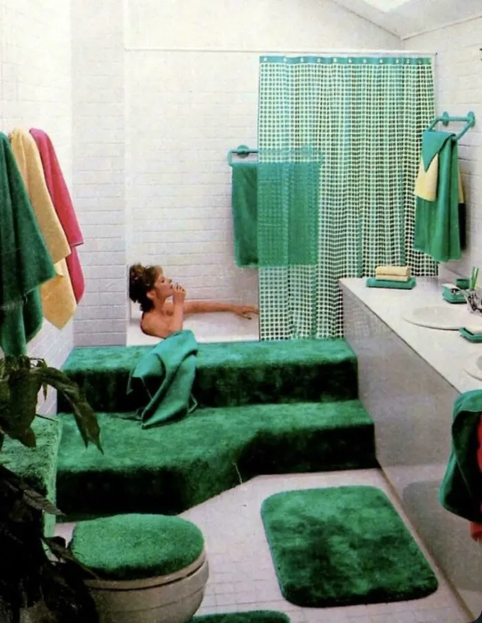 Bathroom with an all-green theme, including a woman bathing in a tub with matching carpeted steps, showcasing 1970s and 1980s interior design.