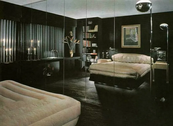A luxurious 1970s and 1980s interior design bedroom with dark walls, a large bed, mirrored closet doors, and modern lighting.
