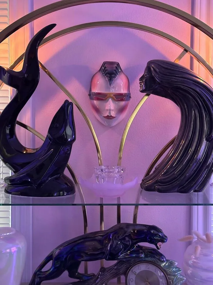 Decorative ceramic sculptures and a face mask embodying 1980s interior design aesthetics on a display shelf.