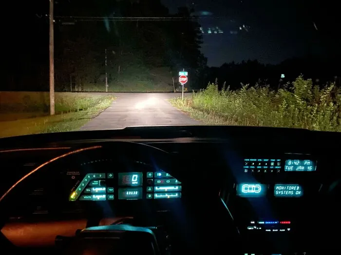 A car's dashboard at night with glowing digital displays, reflecting 1970s and 1980s interior design.