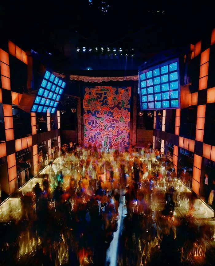 A vibrant 1980s interior design nightclub with a colorful Keith Haring mural and a crowded dance floor, full of energy.