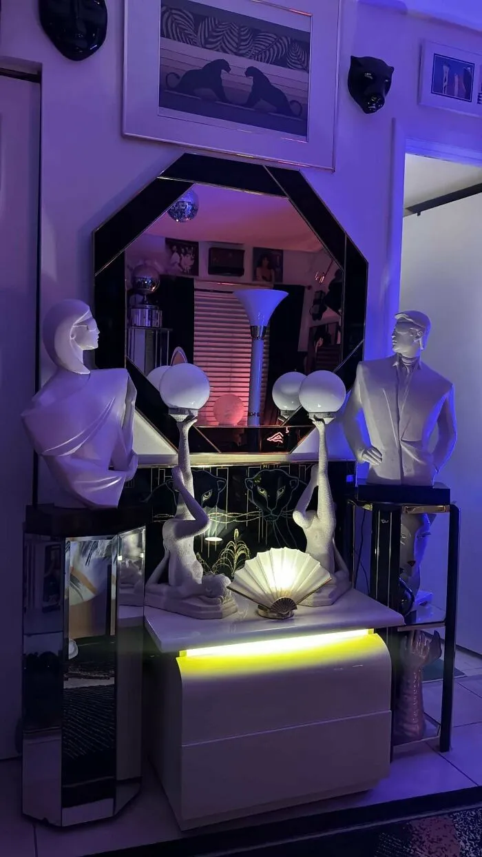 A display of 1970s and 1980s interior design featuring stylized busts, mirrored furniture, and purple lighting.