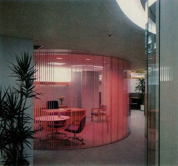 An office meeting room featuring bold 1980s interior design, with curved pink translucent walls and modern furniture.