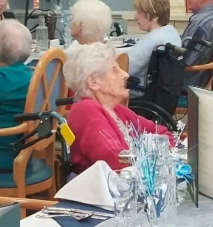 An elderly woman with white hair in a wheelchair at a dining table, part of interesting timeline facts.