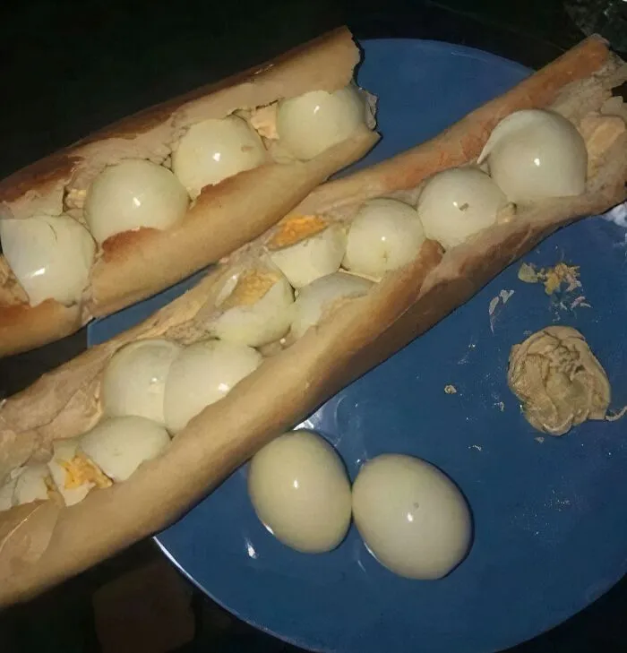 Two baguettes filled with numerous hard-boiled eggs on a blue plate, a piece of stupid and disgusting food.