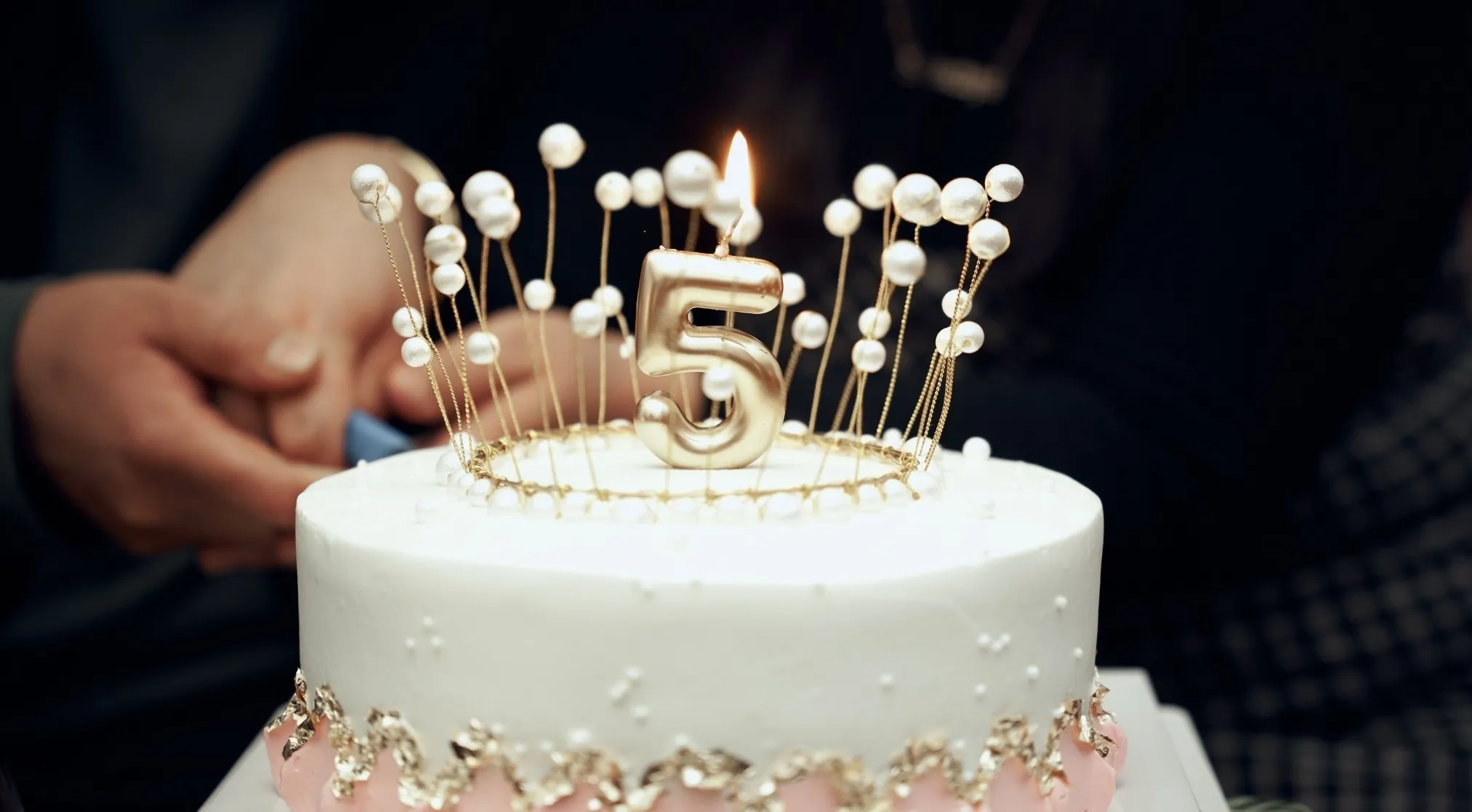 A white birthday cake with a lit number 5 candle, surrounded by pearl decorations. A 1% Club question.