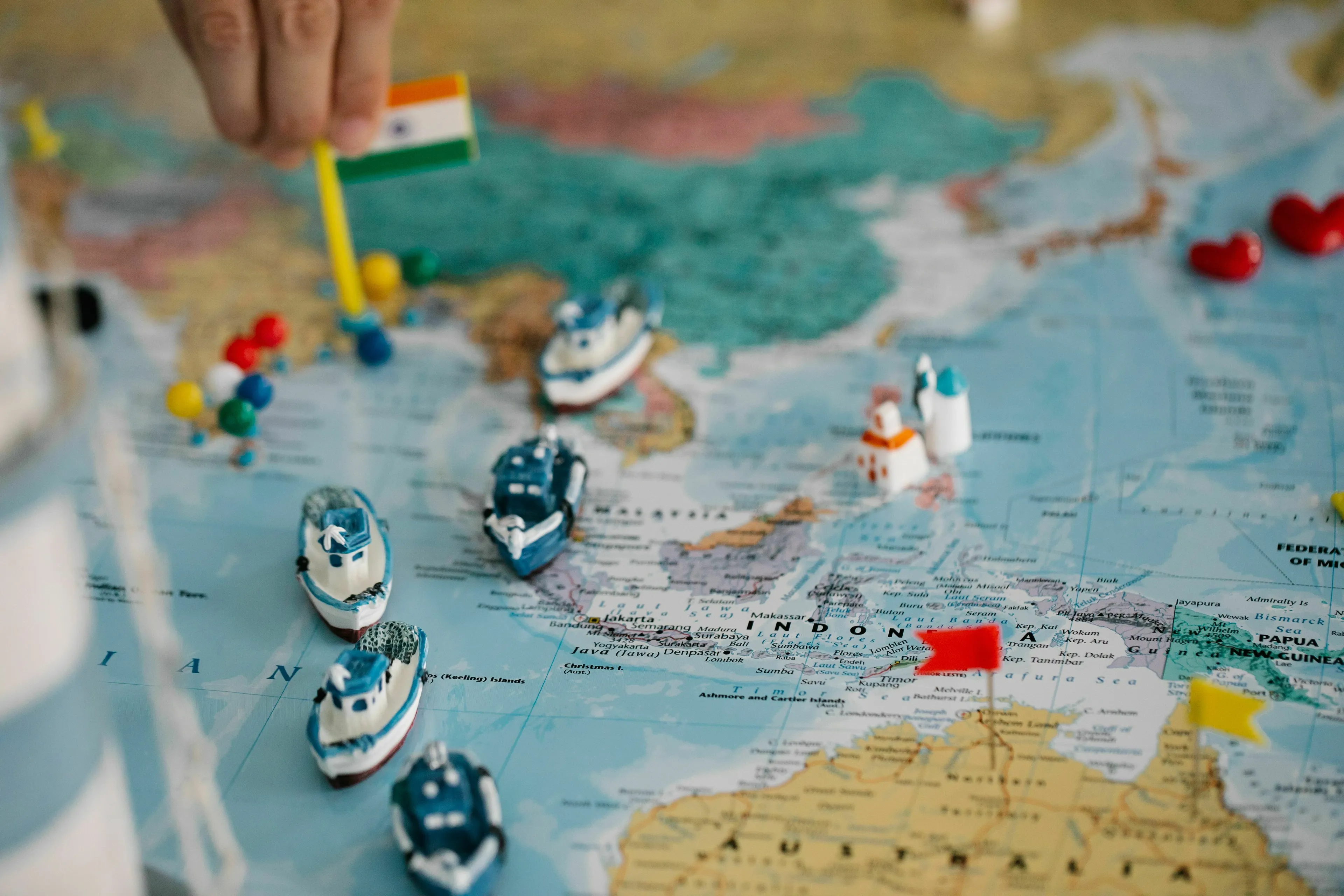 A hand places an Indian flag on a world map with toy boats, ideal for an odd one out general knowledge challenge.