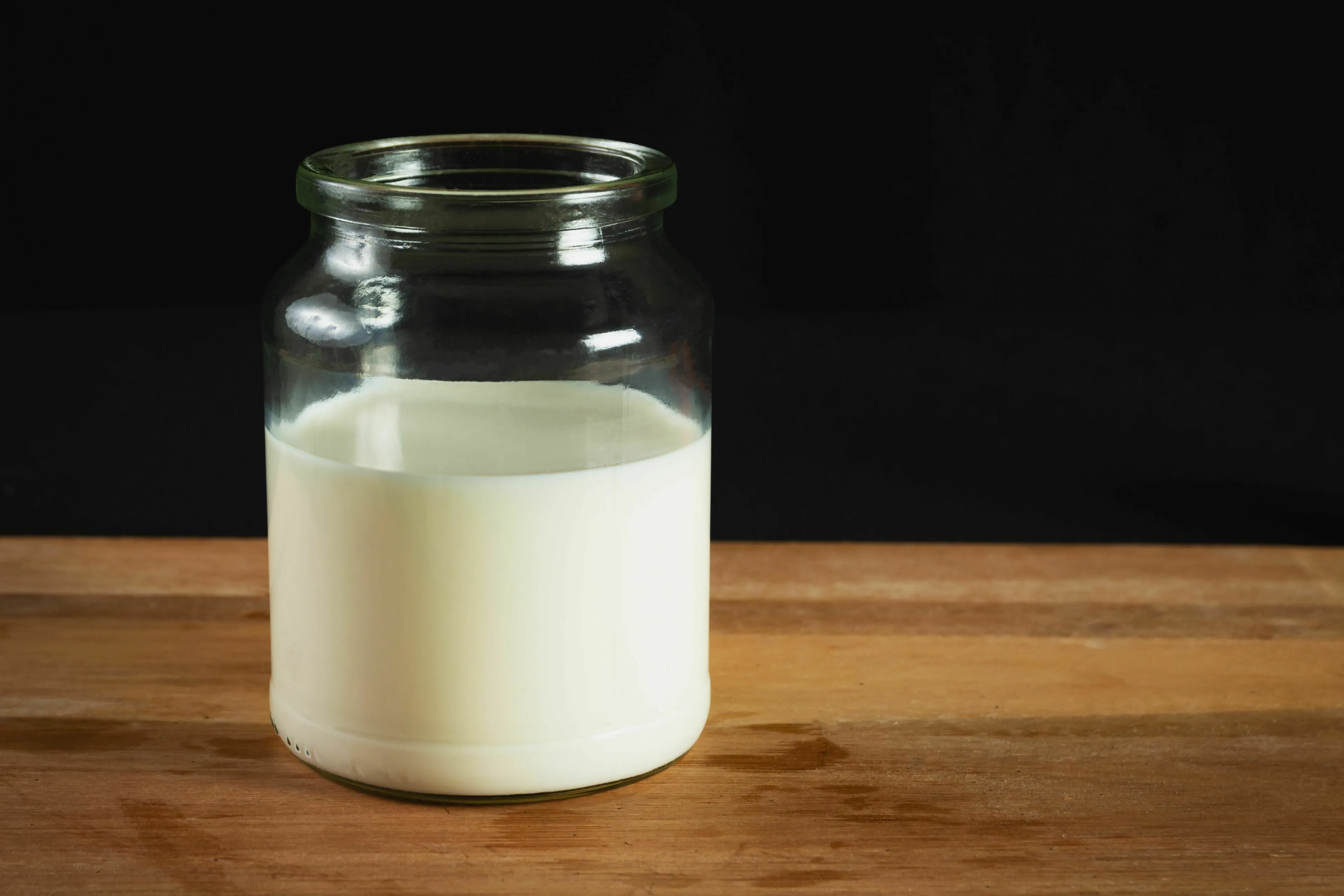 A glass jar half-filled with milk on a wooden surface, ready for a pick the odd one out general knowledge challenge.