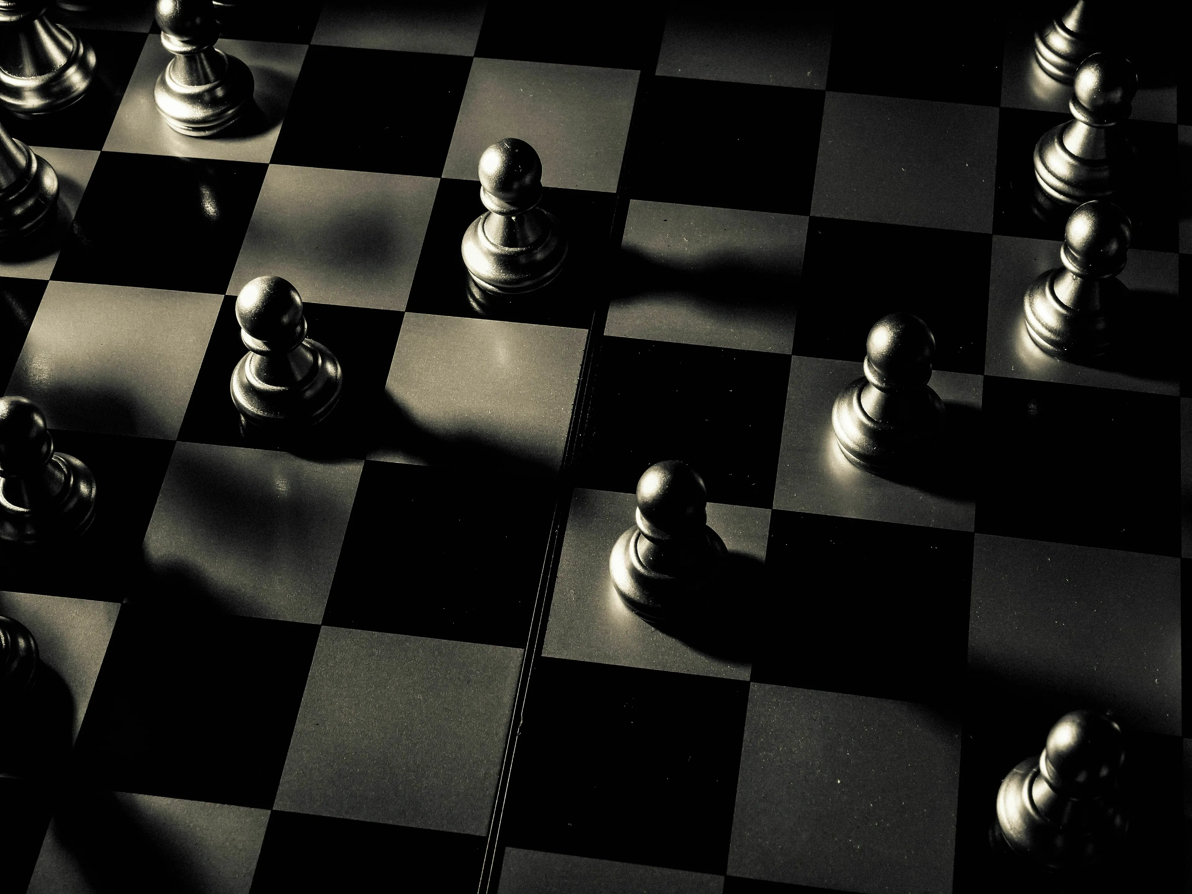 A chessboard with several chess pieces in a dark, moody light, challenging to find the odd one out.