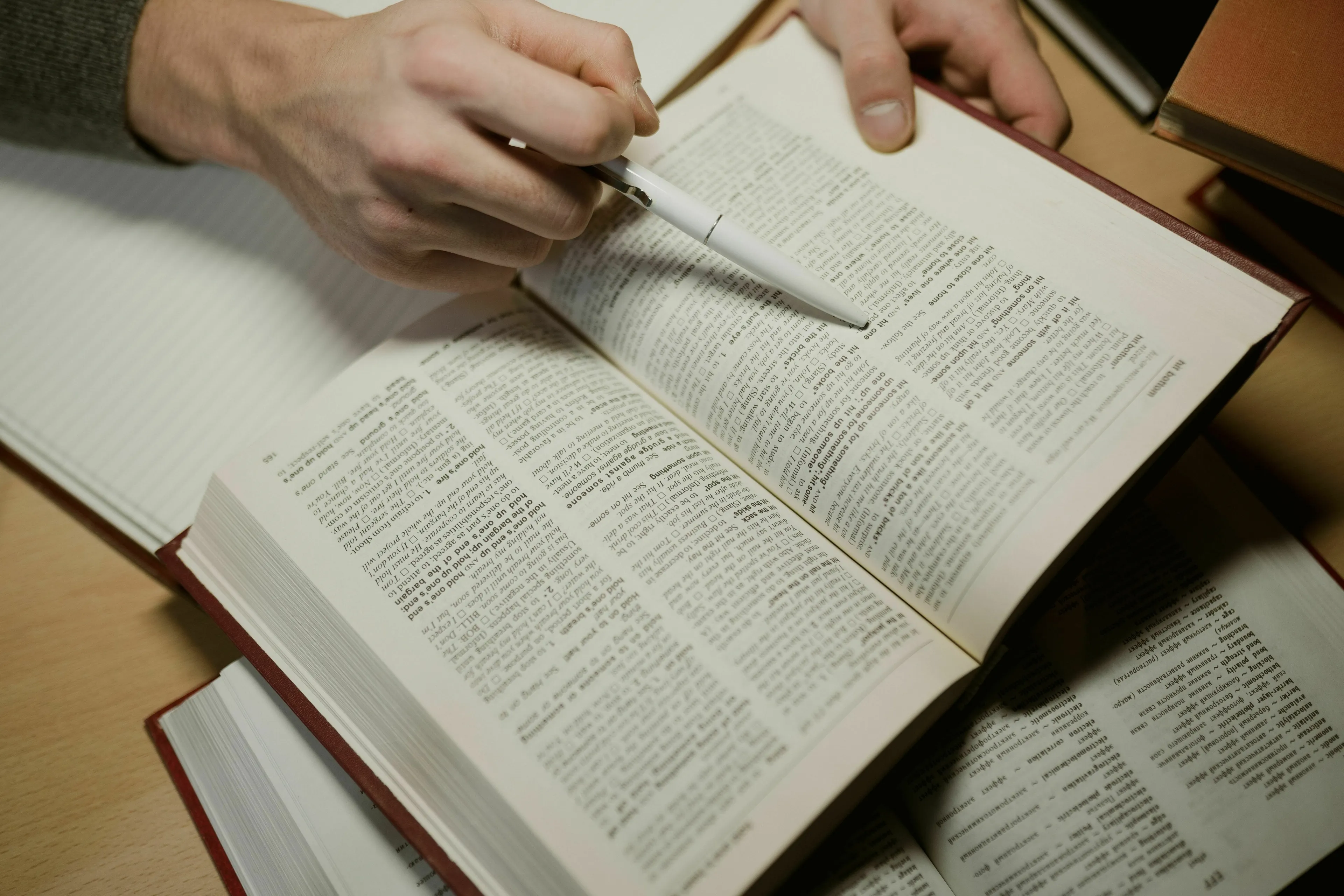 Two hands holding open a book, with one hand pointing at the text with a pen for an odd one out general knowledge challenge