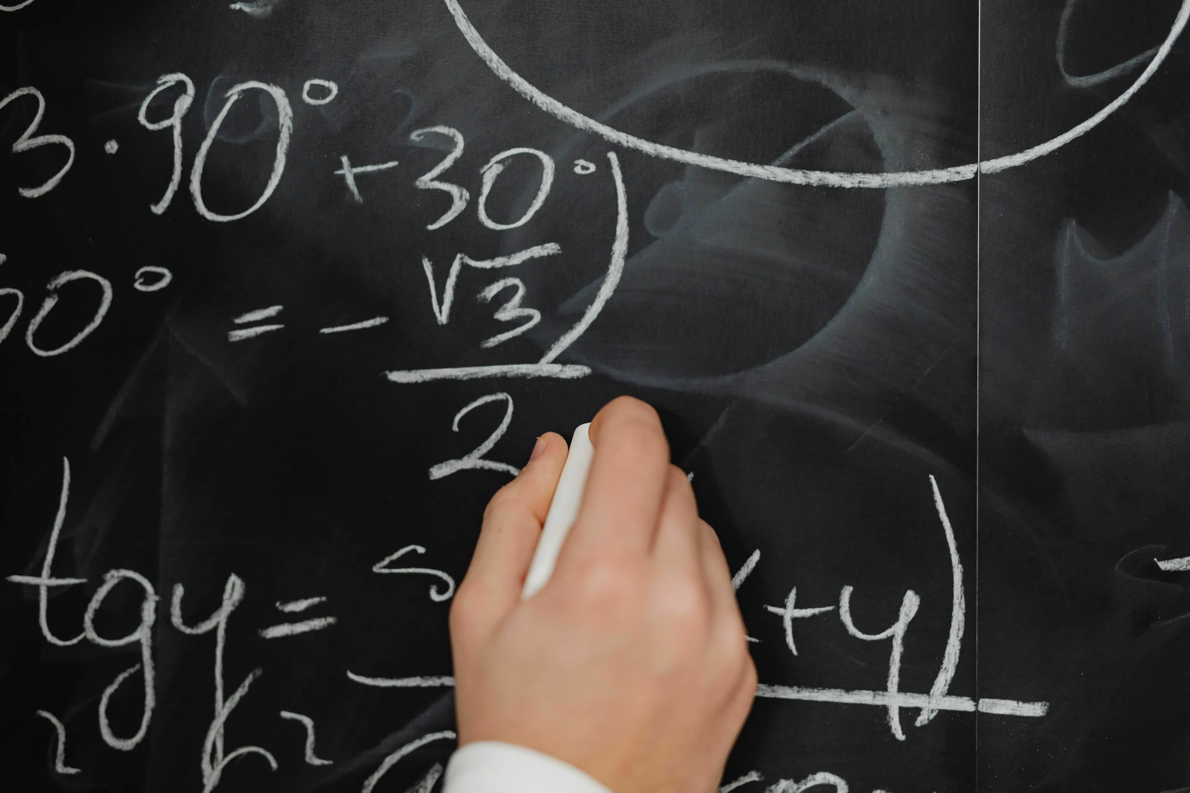 A hand writing mathematical equations on a chalkboard for a general knowledge challenge to spot the intruder.