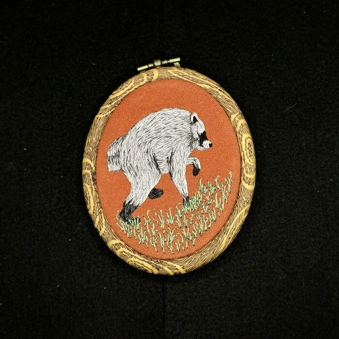 An embroidery project depicting a raccoon walking in green grass