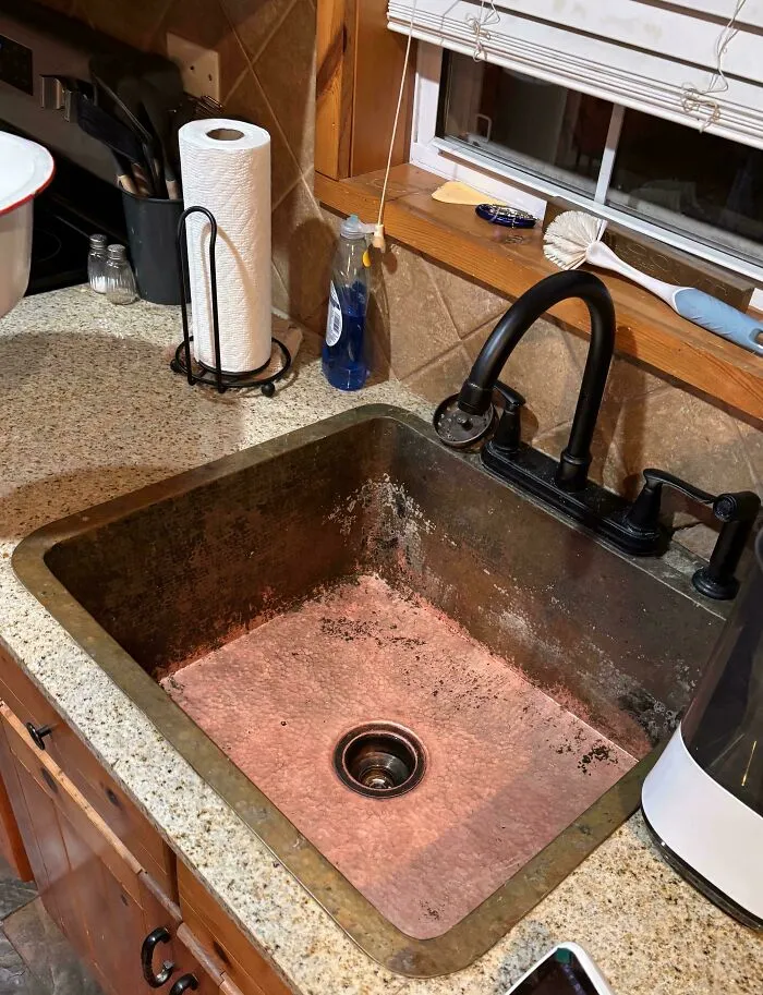 A dirty kitchen sink that needs fixing things. The sink is made of copper and has a dark patina.