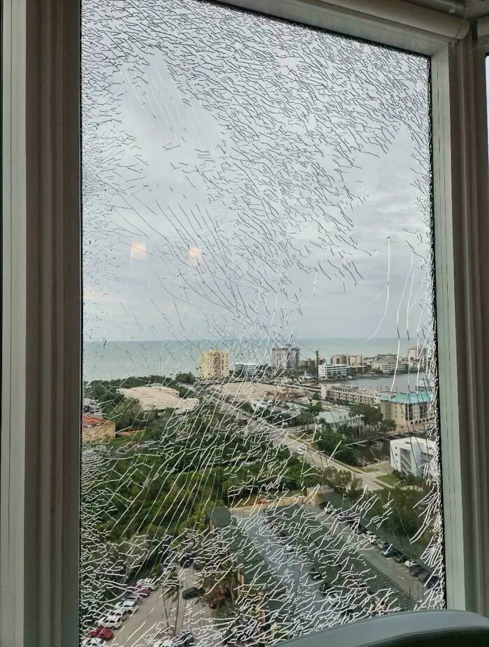 A shattered window looking out onto a cityscape and ocean, needing help fixing things and finding answers to problems.