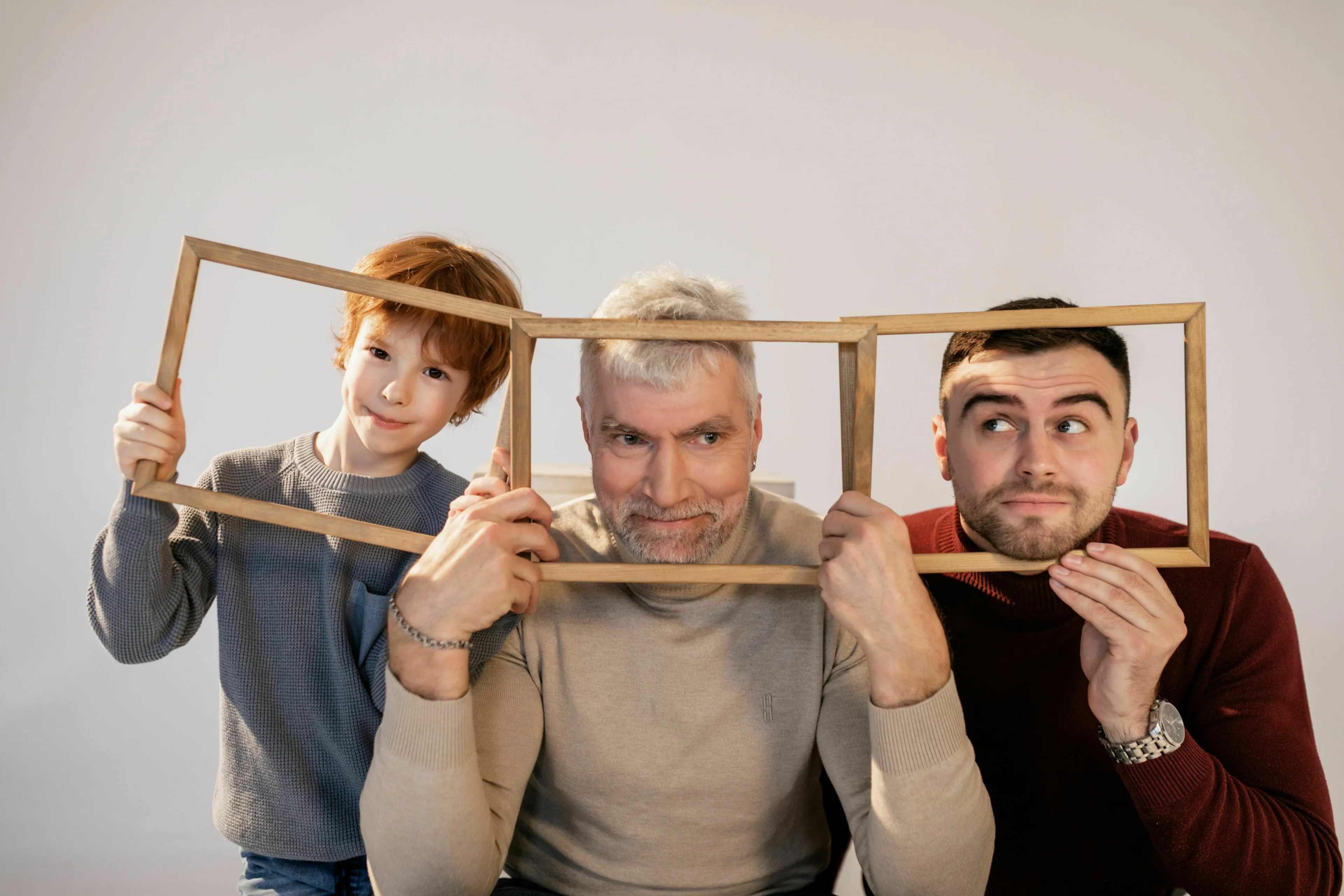 A multi-generational family, three males, poses for tricky questions. The grandfather is in the middle with his son and grandson.