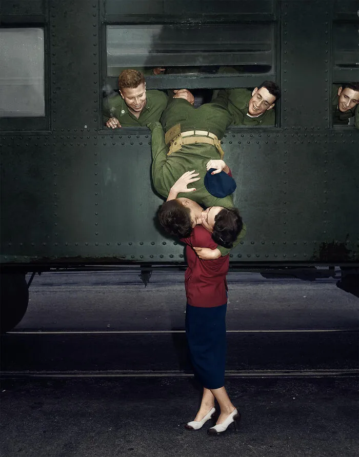 Historical photo of a soldier hanging upside down from a train window to kiss a woman goodbye, capturing a poignant past moment.