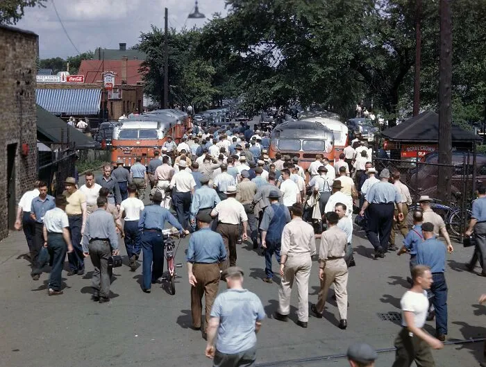 A crowded street scene with many people walking, two buses, and buildings in the background, captured in historical photos.