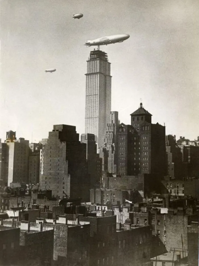 Historical photo showing three airships flying over skyscrapers in a bustling city, capturing a past moment.