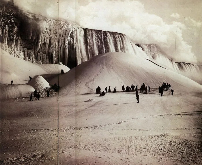 Historical photos: People walk on a snow-covered landscape with a frozen Niagara Falls in the background, a winter past.