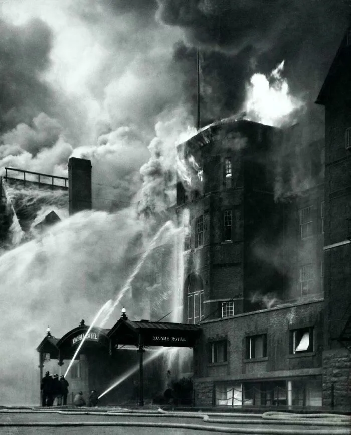 Historical photo of a building engulfed in flames, with firefighters battling the blaze.