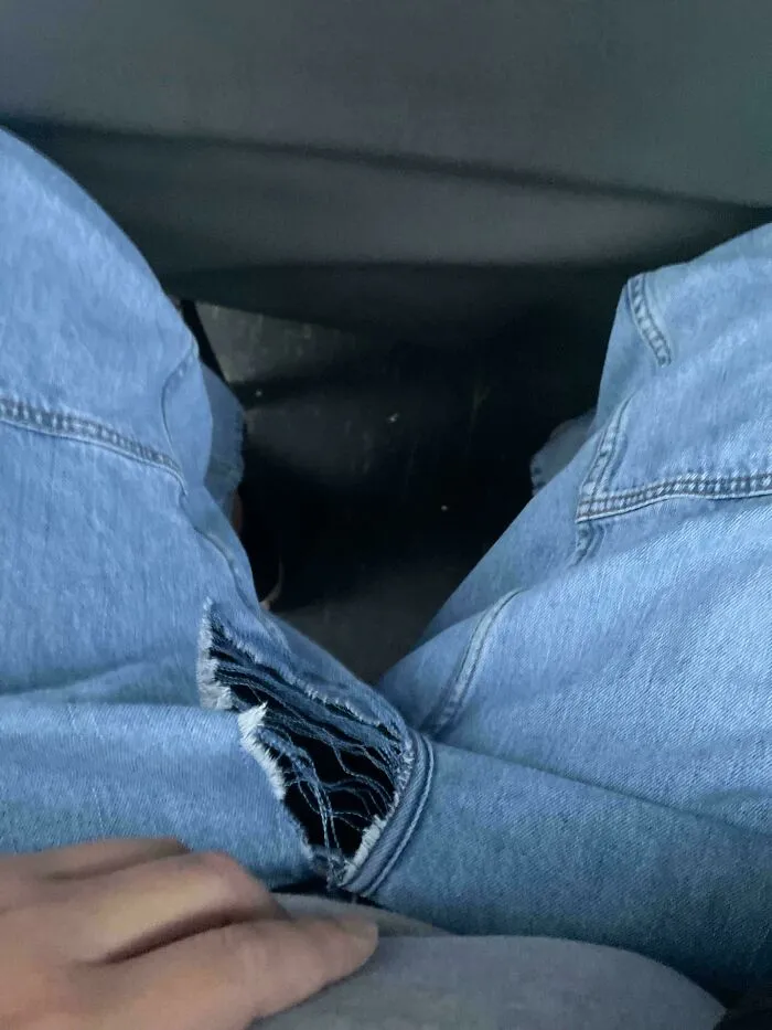A person's legs in ripped blue jeans, sitting with a tear near the crotch, a common problem needing fixing things.