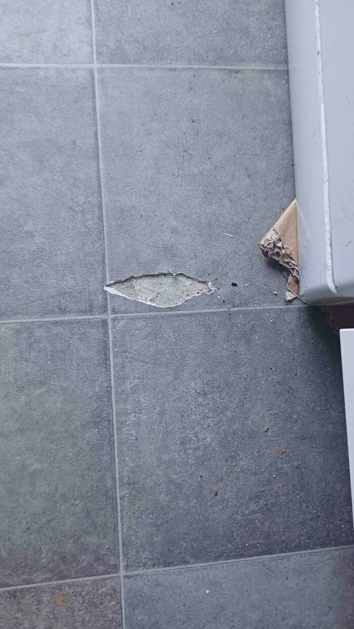 A damaged section of a grey tiled floor where a piece of tile has broken off, indicating a problem needing fixing.