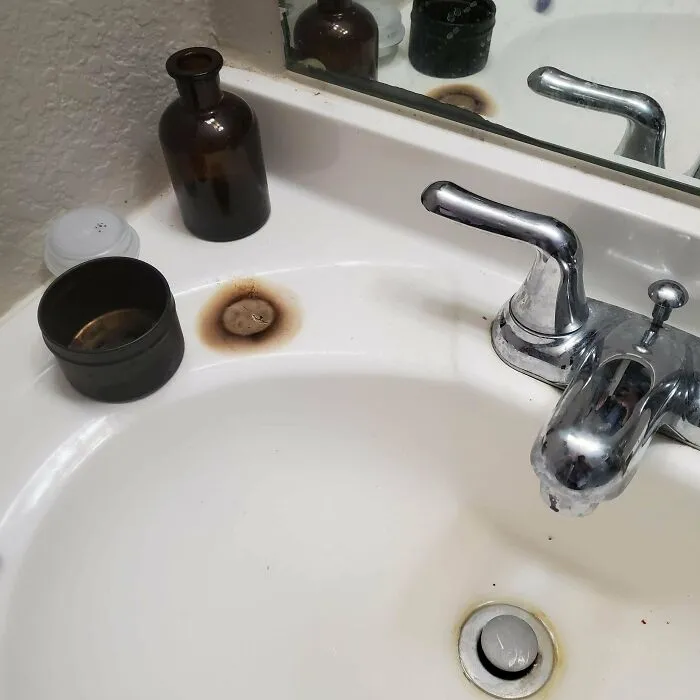 A bathroom sink with a rusted spot near the faucet, indicating a common household problem that people often ask others for help fixing.