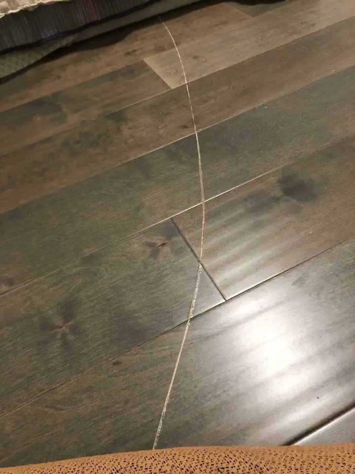 A close-up of a long, thin scratch on dark wood flooring, showing a common problem people ask others for help fixing things.