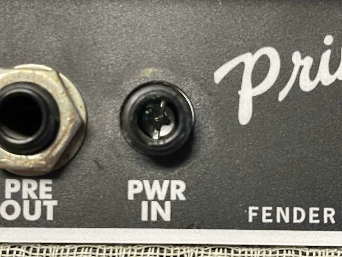 A close-up of an amplifier's back panel, showing the PWR IN jack and other connections, highlighting a problem to fix.