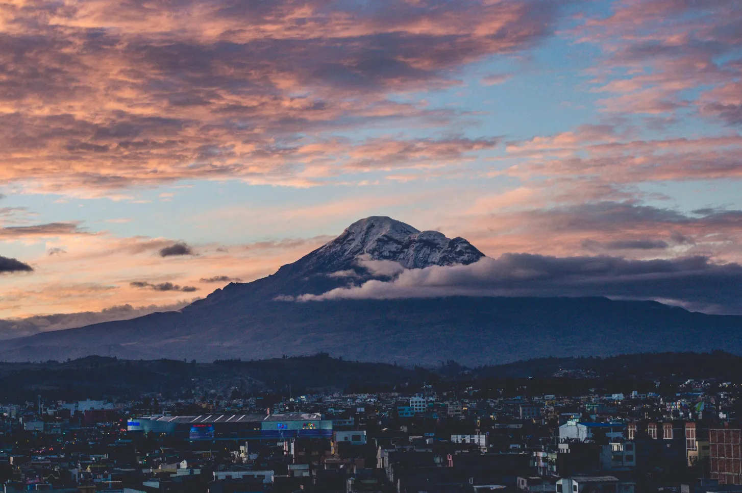 Mount Chimborazo, Ecuador, closest to moon and outer space, majestic peak rising above a city at sunset with dramatic clouds.