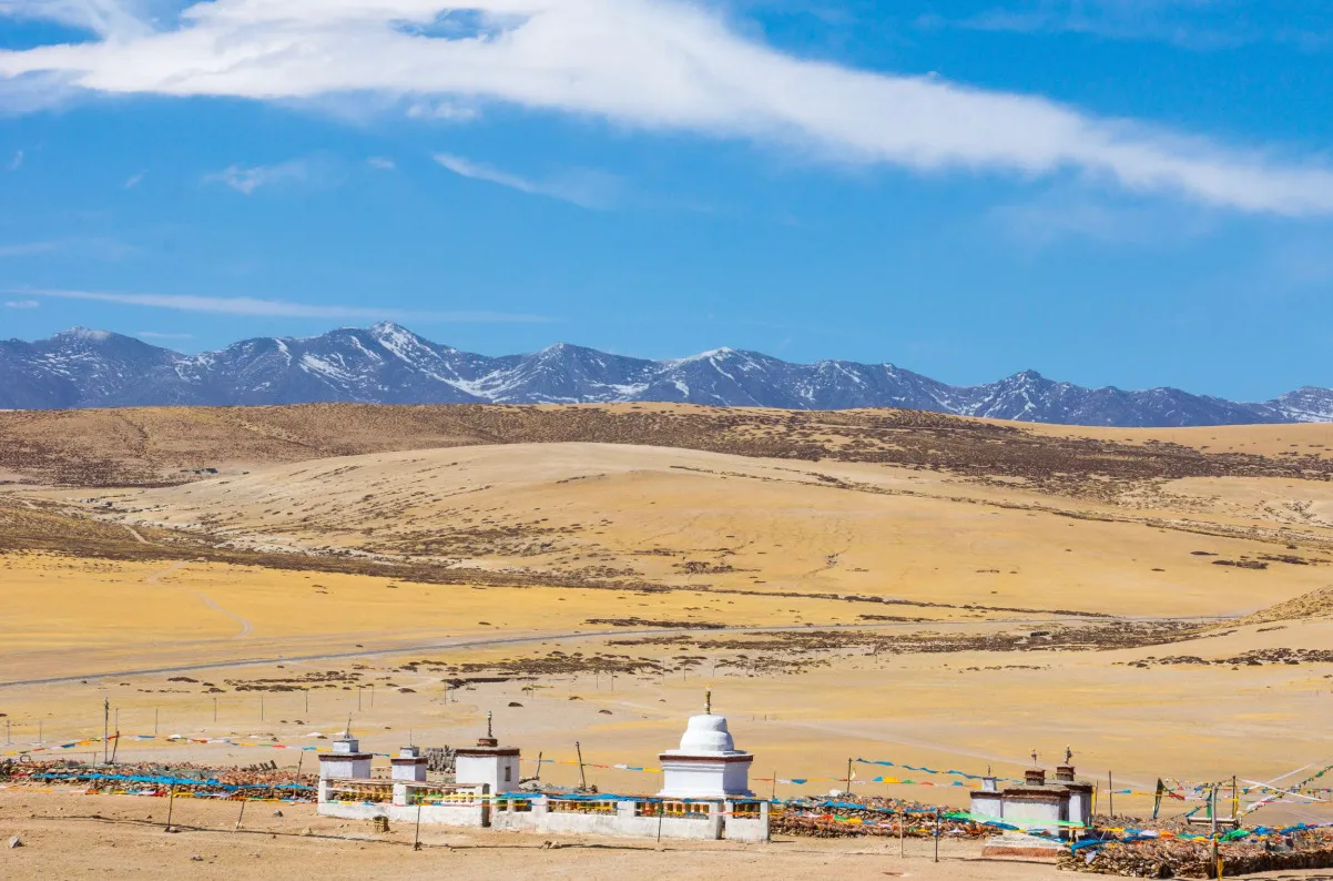 Tibetan Plateau, closest to moon and outer space, vast dry landscape with distant snow-capped mountains and prayer flags.