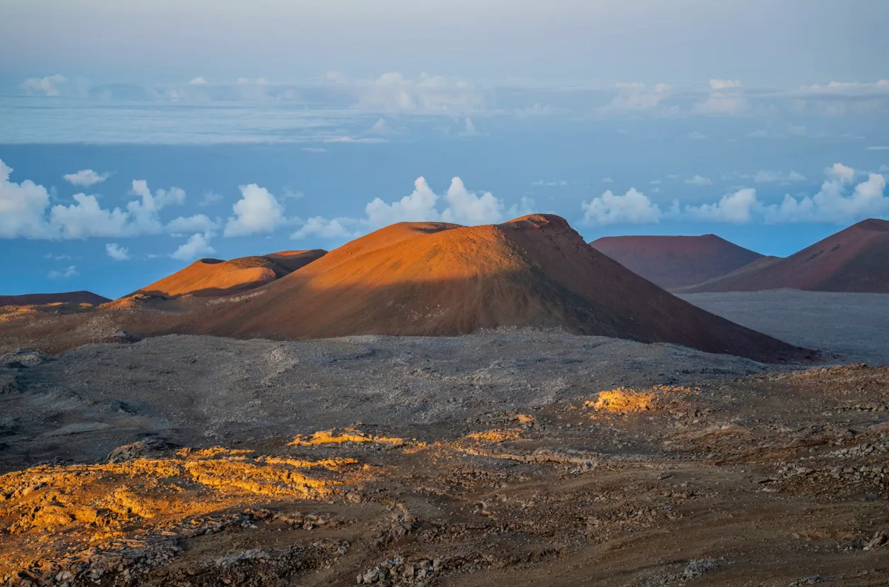 Mauna Kea, Hawaii, closest to moon and outer space, volcanic landscape with reddish craters under a partly cloudy sky.