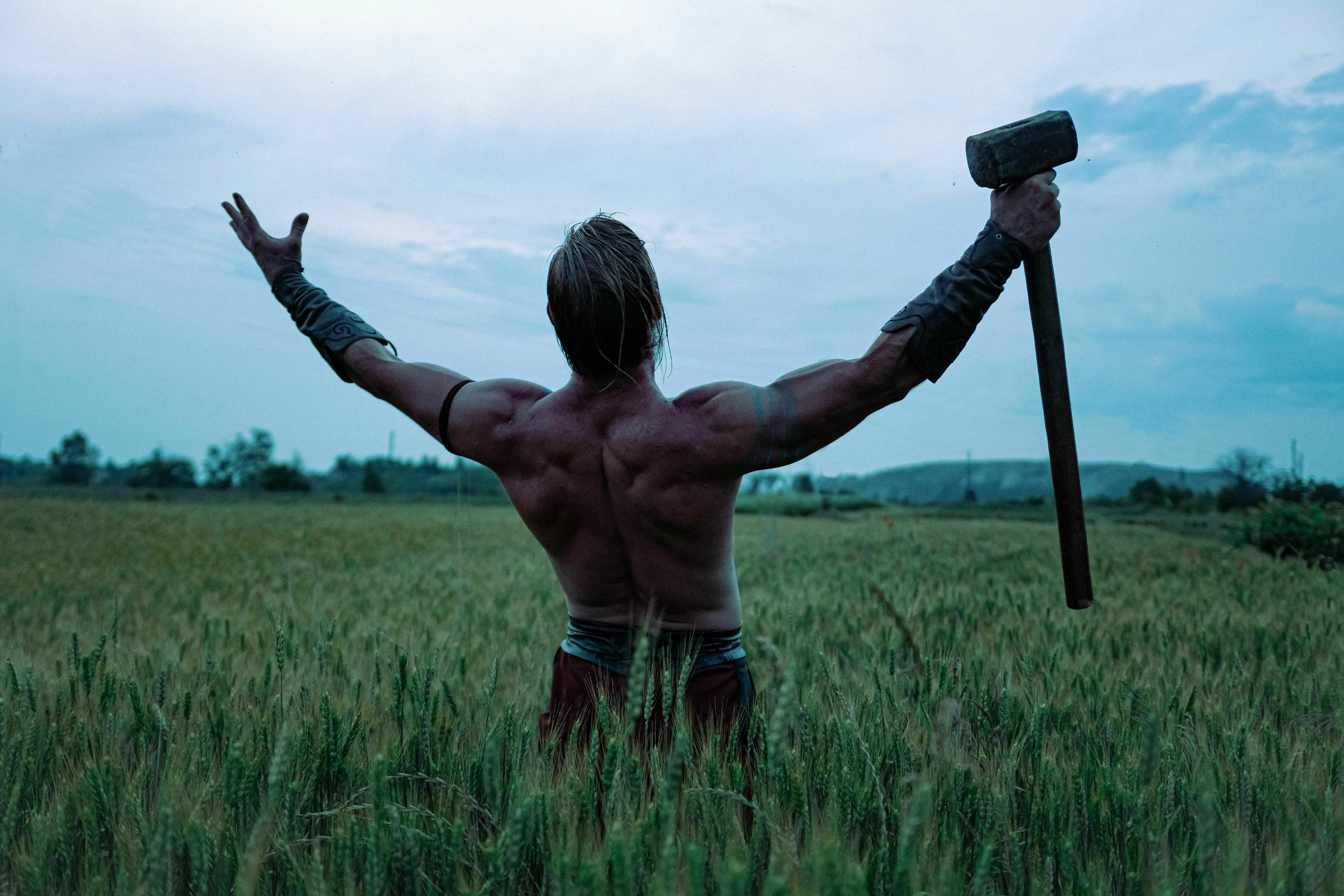 A muscular man, back to the camera, holding a hammer in a field. This image is for a general knowledge quiz.