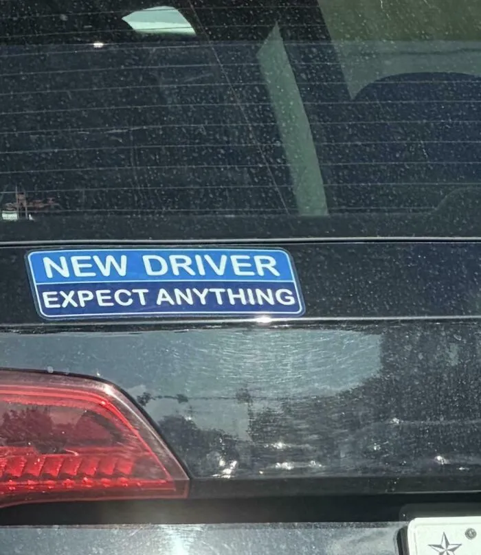 A funny bumper sticker on a car's rear that says, NEW DRIVER EXPECT ANYTHING.